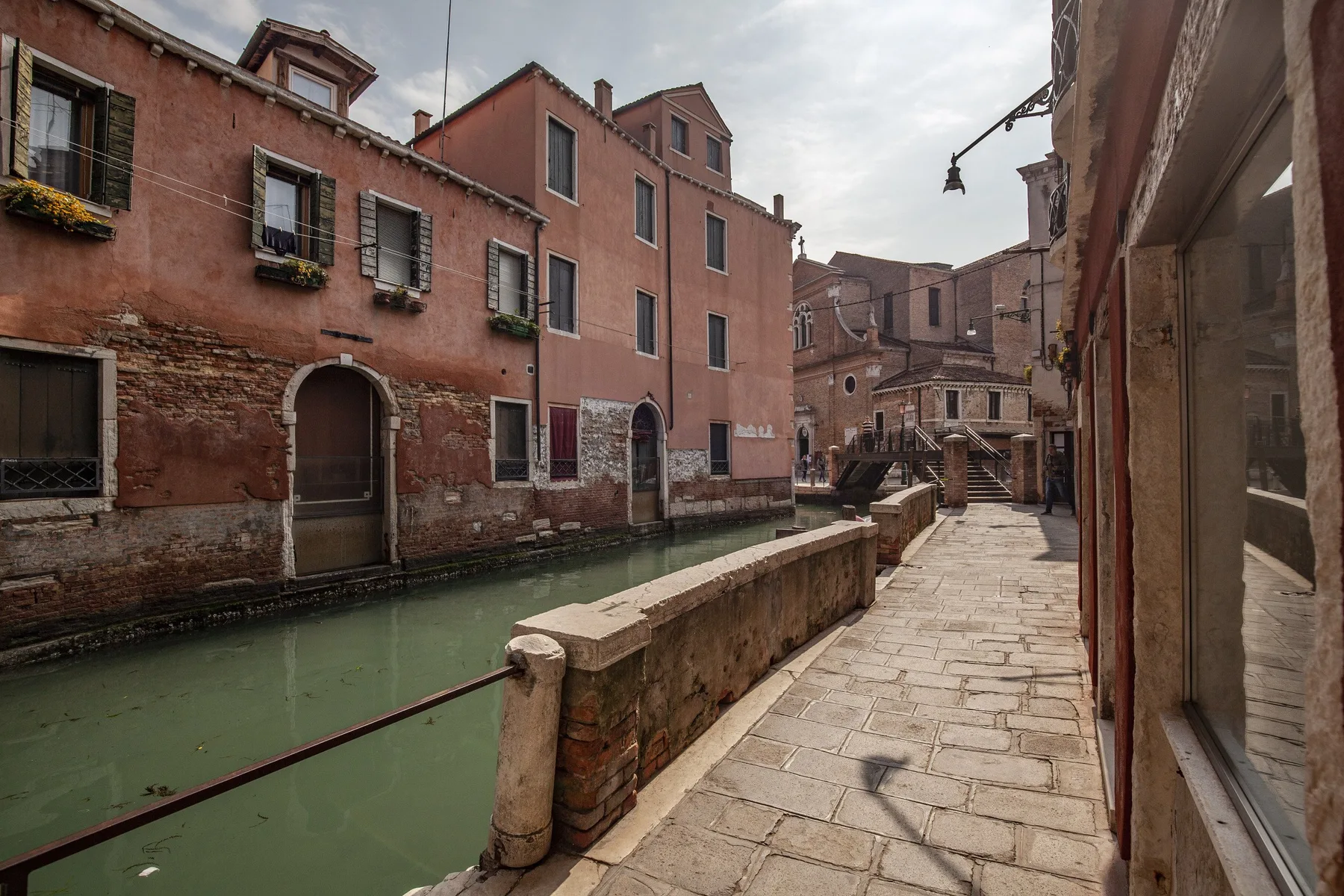 A stone walkway runs beside a green canal between closely spaced buildings.