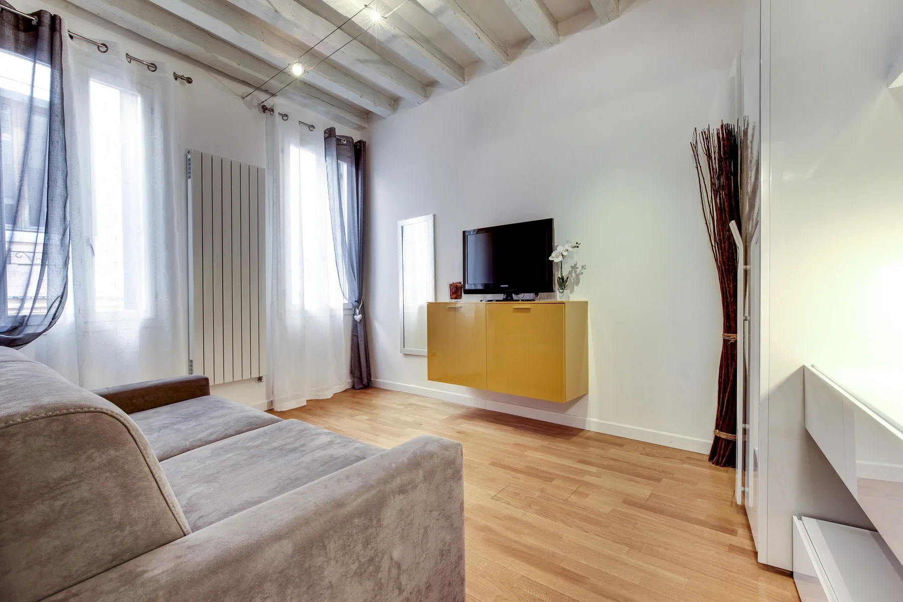 A bright living room with seating, a television, and a wall-mounted cabinet.