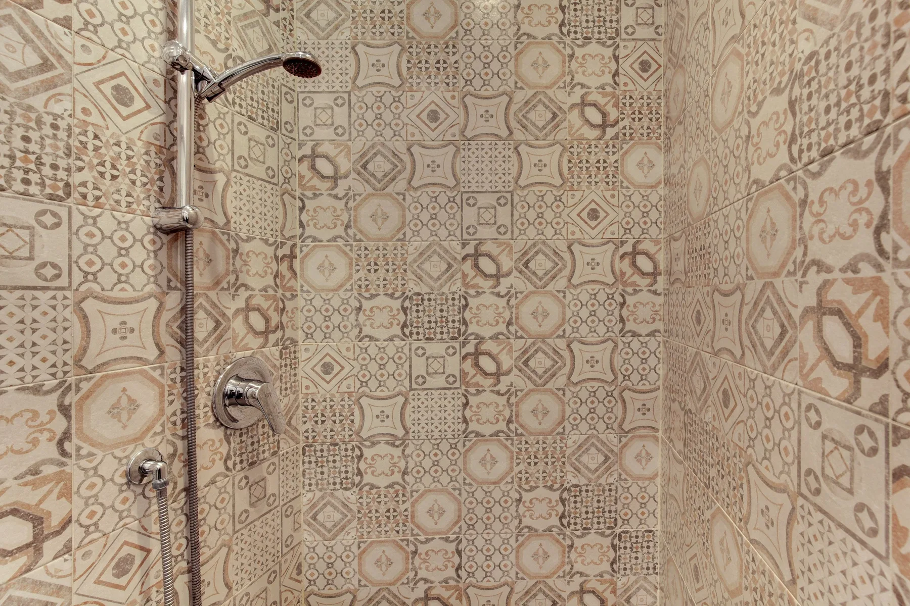 A tiled shower with a wall-mounted showerhead and patterned walls.