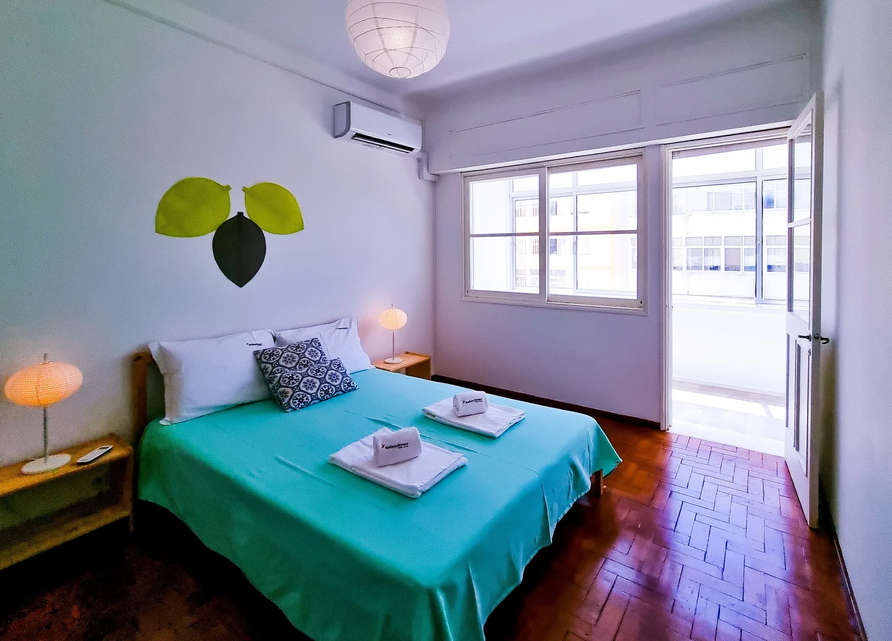 Dormitorio con cama doble, ropa de cama turquesa y una puerta abierta al balcón.