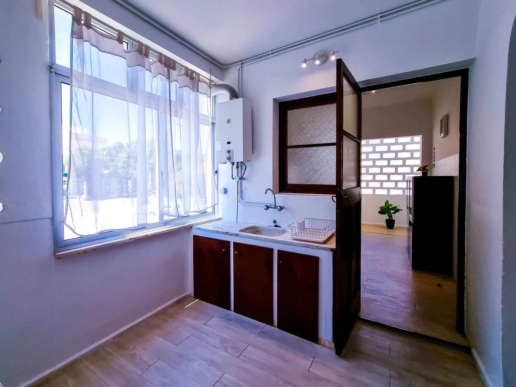 Una cocina pequeña con fregadero está junto a una ventana grande con cortinas.