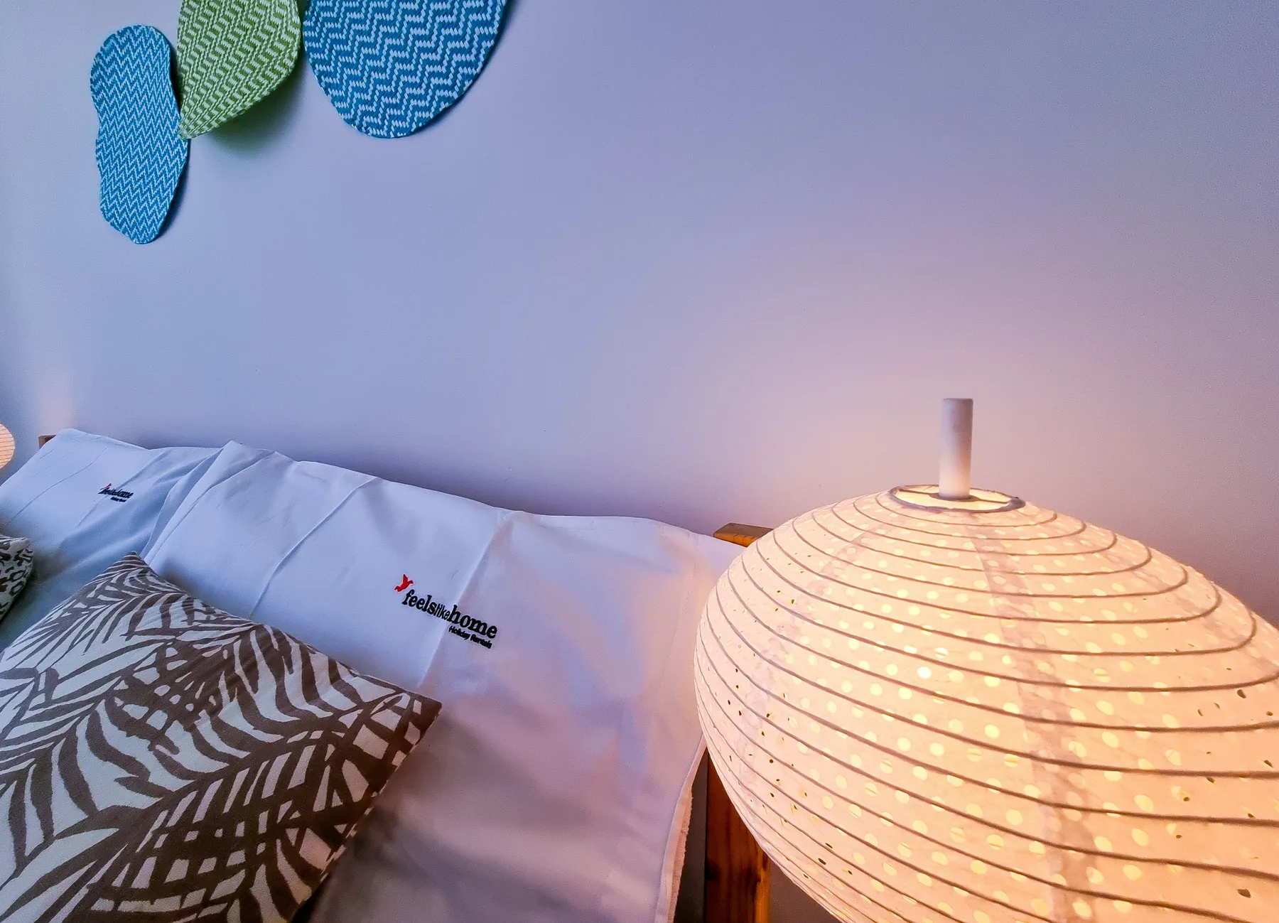 Dormitorio con cama, cojines estampados y una lámpara encendida.