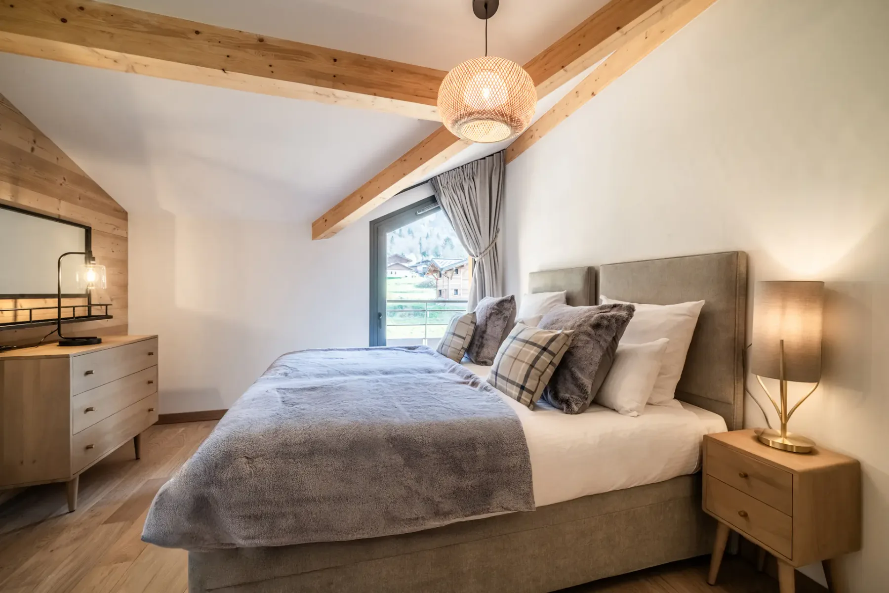 Modern bedroom and bathroom with wooden accents; the bathroom has a bathtub and a large window with a mountain view.