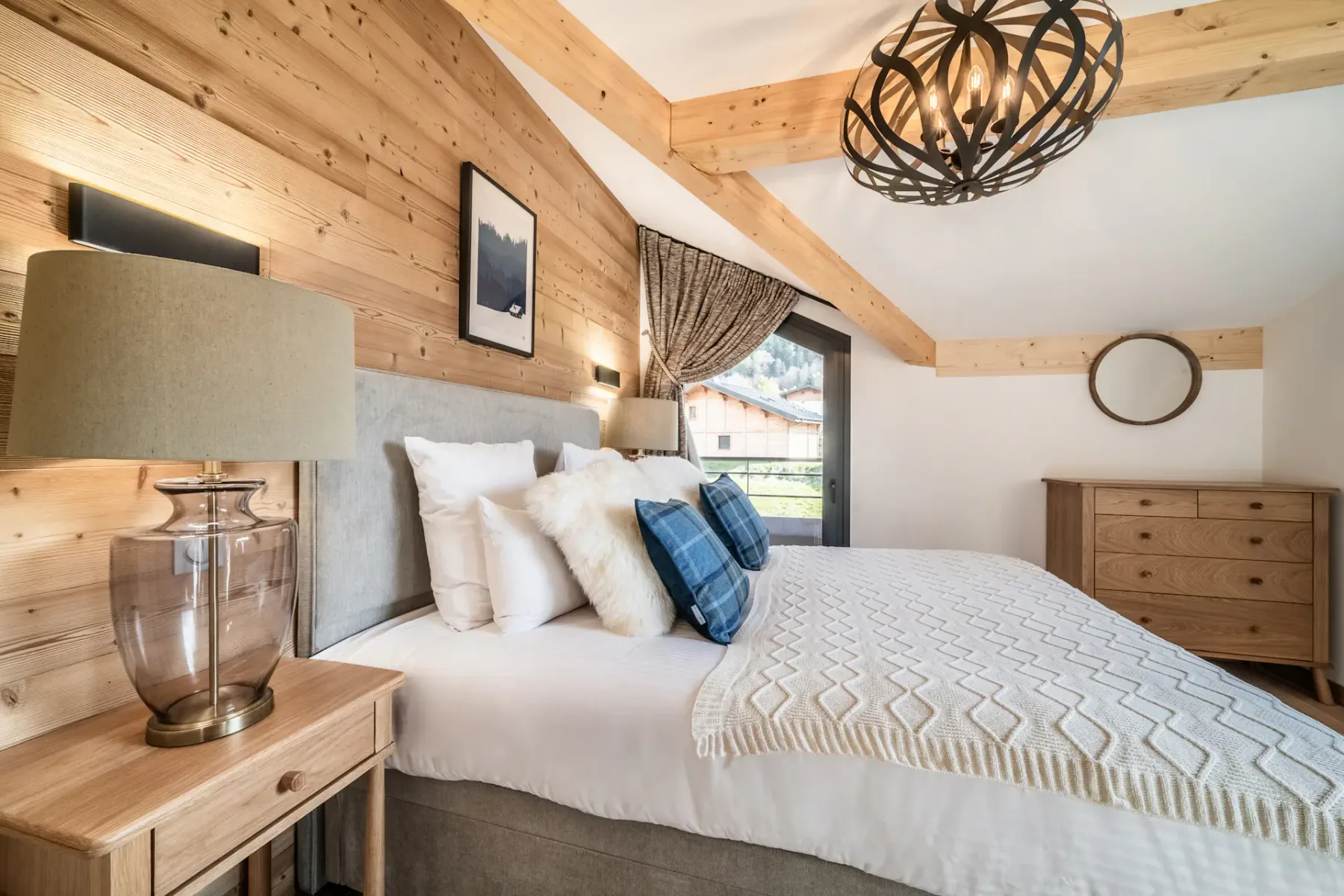 Modern bedroom and bathroom with wooden accents; the bathroom has a bathtub and a large window with a mountain view.