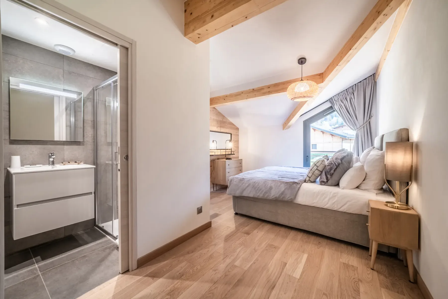 Modern bedroom and bathroom with wooden accents; the bathroom has a bathtub and a large window with a mountain view.