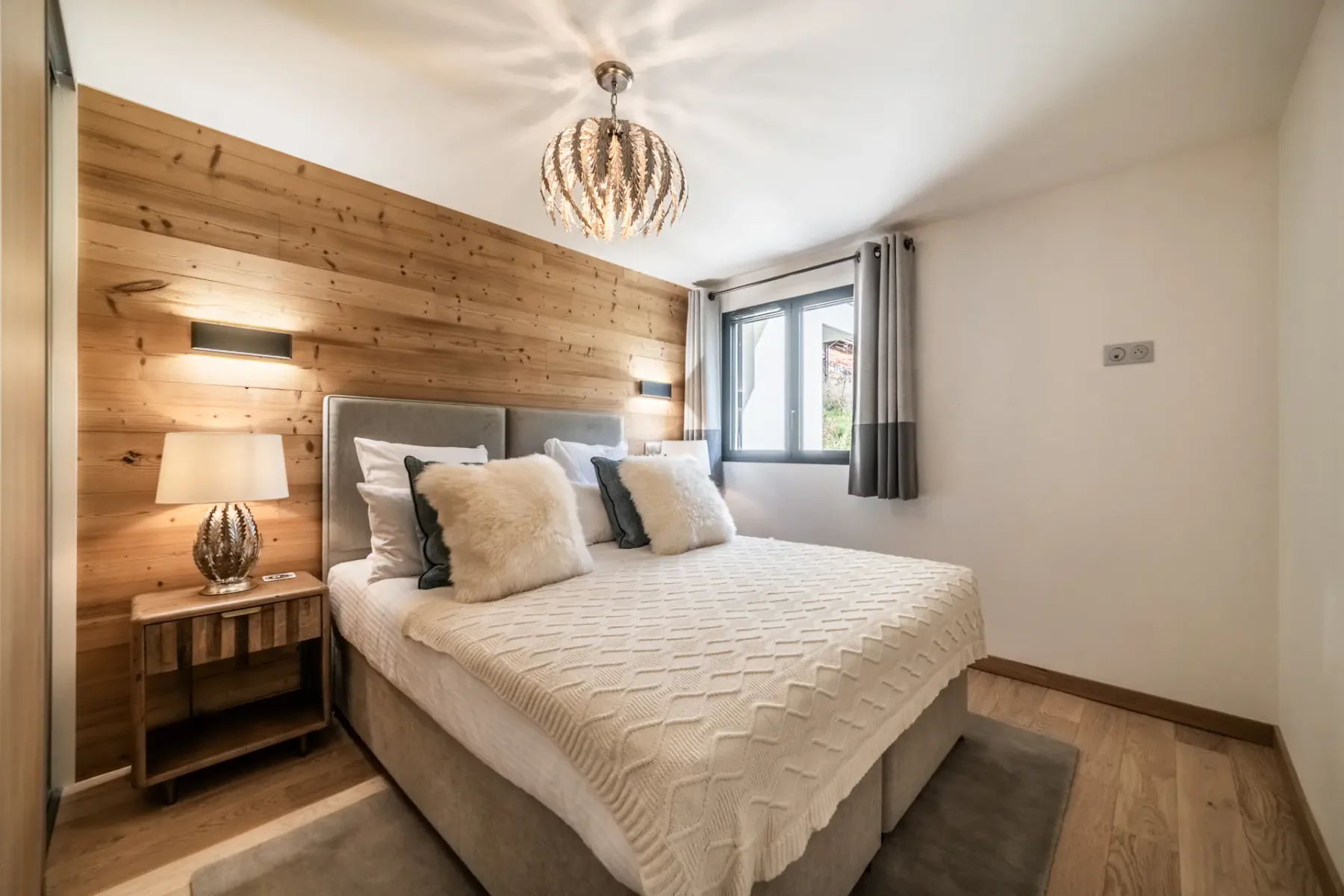 Modern bedroom and bathroom with wooden accents; the bathroom has a bathtub and a large window with a mountain view.