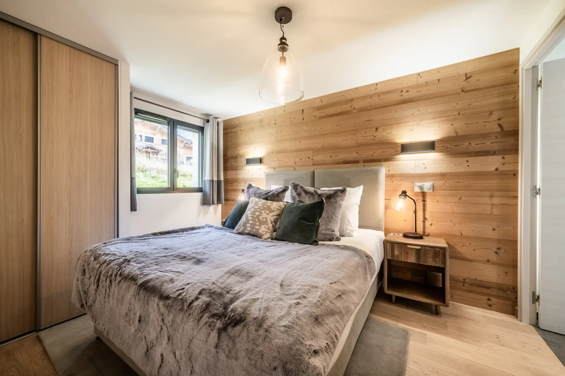 Modern bedroom and bathroom with wooden accents; the bathroom has a bathtub and a large window with a mountain view.
