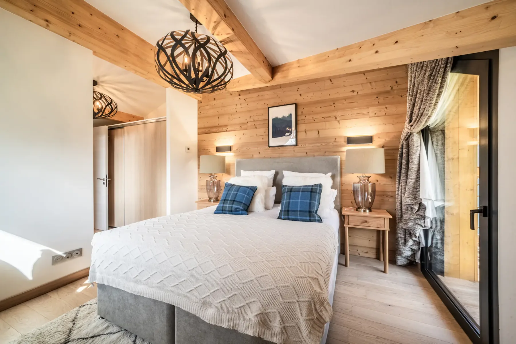 Modern bedroom and bathroom with wooden accents; the bathroom has a bathtub and a large window with a mountain view.