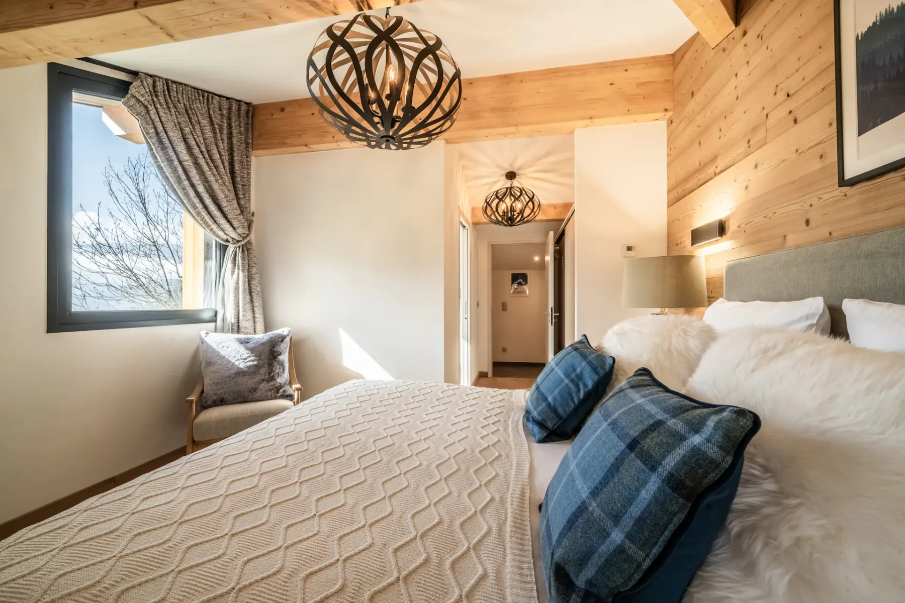 Modern bedroom and bathroom with wooden accents; the bathroom has a bathtub and a large window with a mountain view.