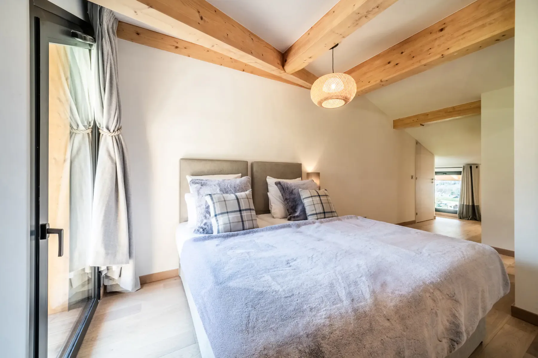 Modern bedroom and bathroom with wooden accents; the bathroom has a bathtub and a large window with a mountain view.