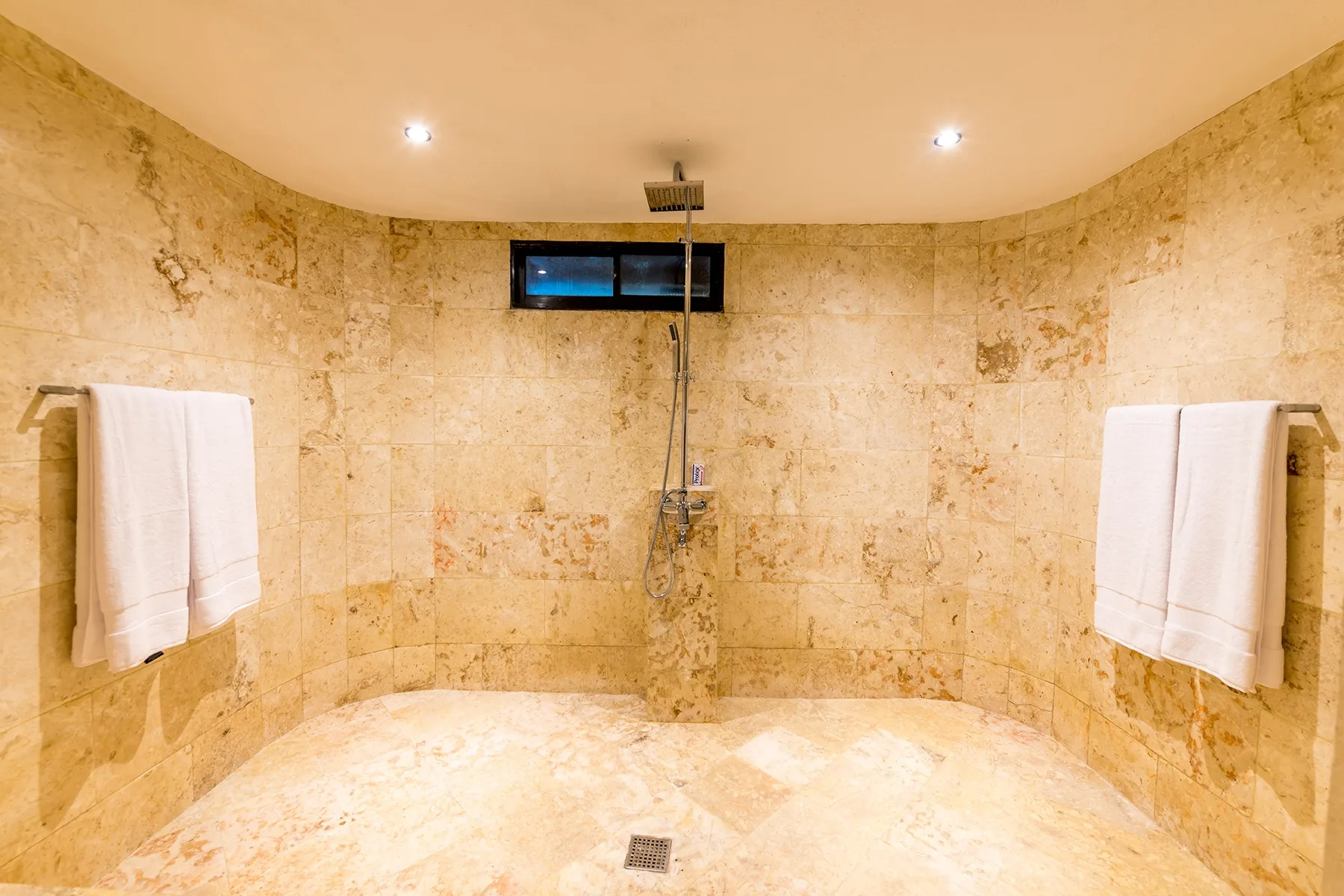 Una zona de ducha revestida con azulejos, con una ducha de pared y toallas colgadas.