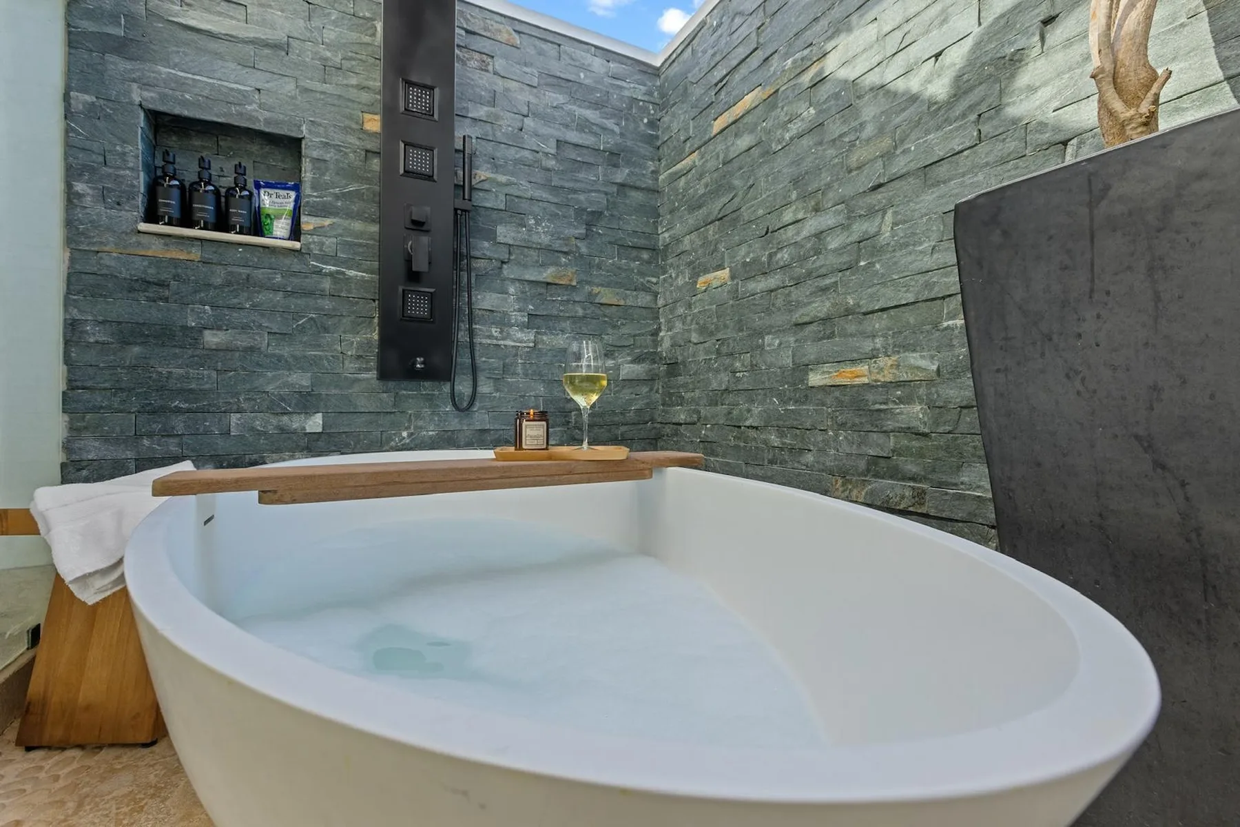 Una bañera está en un baño con paredes de piedra y una copa de vino cerca.