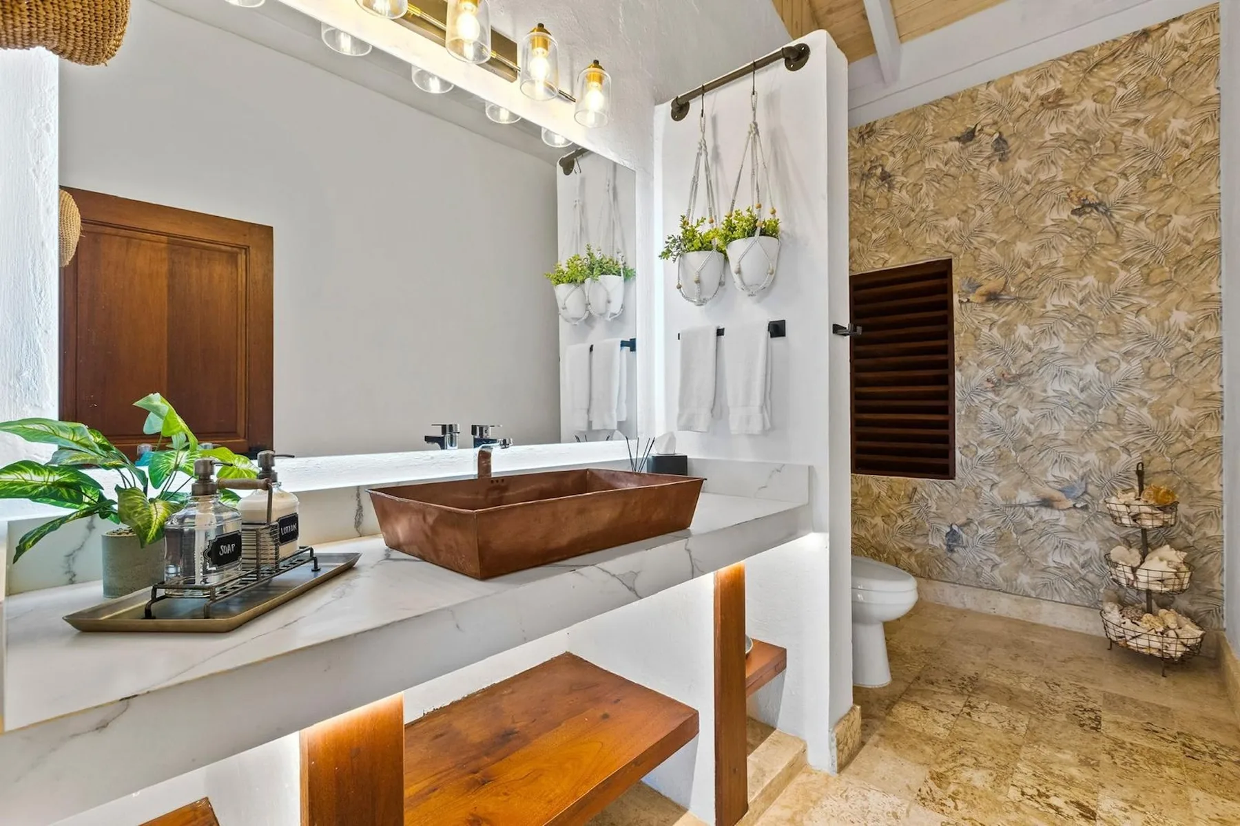 Un tocador de baño con un lavabo de cobre está junto a una zona de ducha con paredes de piedra.