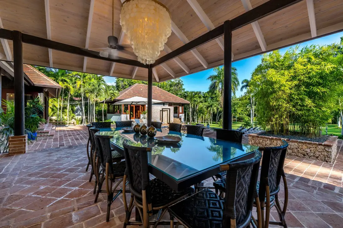 Comedor exterior cubierto con una mesa larga y vegetación alrededor.