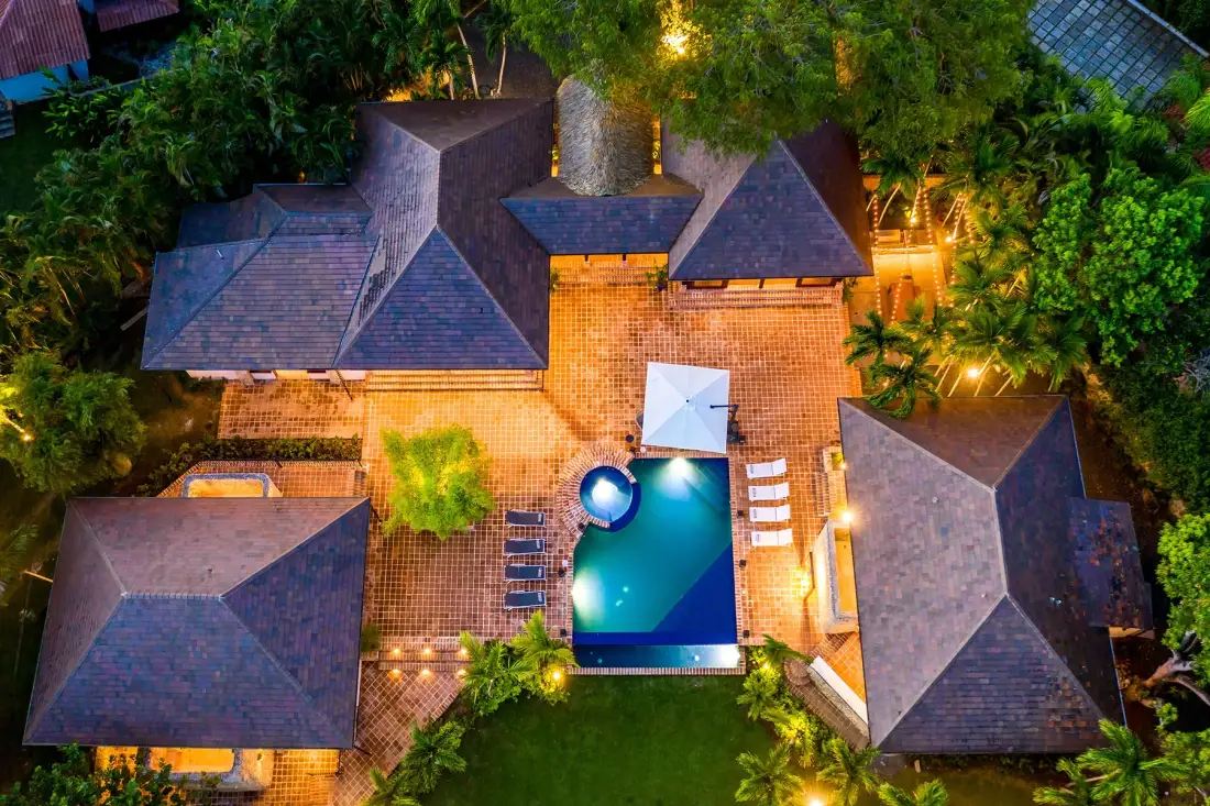 Vista aérea de una piscina rodeada de patios pavimentados y vegetación.