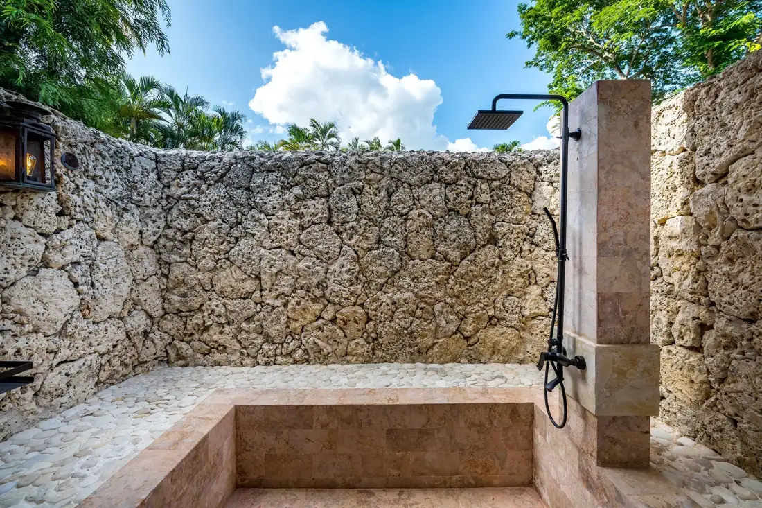 Una ducha al aire libre con una pared de piedra y una plataforma elevada con azulejos.