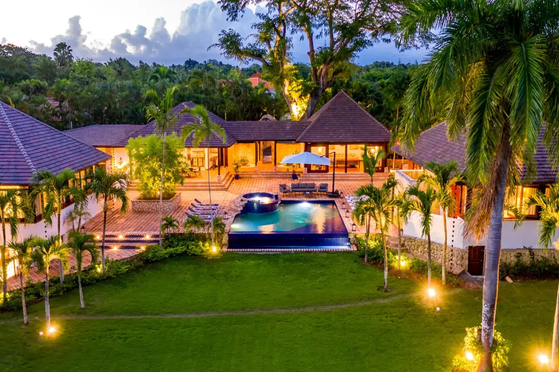 Un resort tropical iluminado rodea una piscina y un césped.