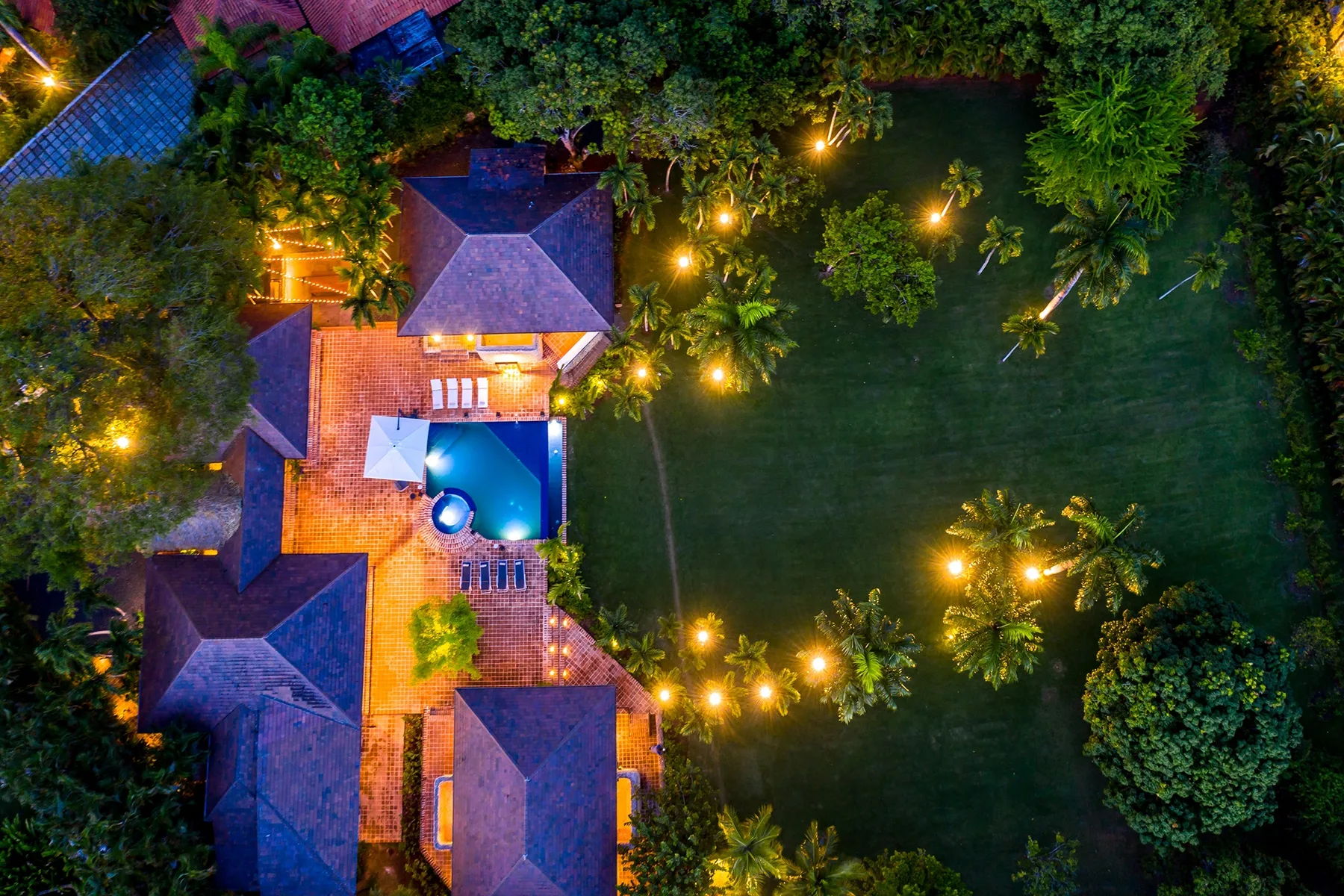 Vista aérea de una propiedad iluminada con piscina y jardines por la noche.