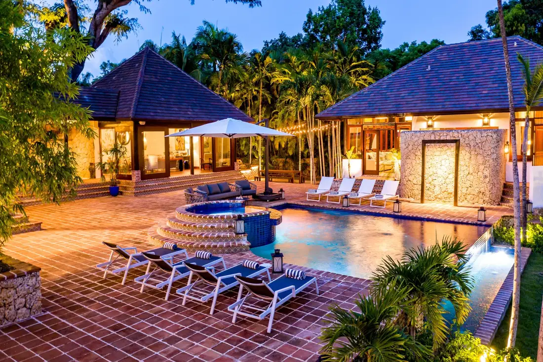 Un patio con piscina, asientos y edificios iluminados al anochecer.