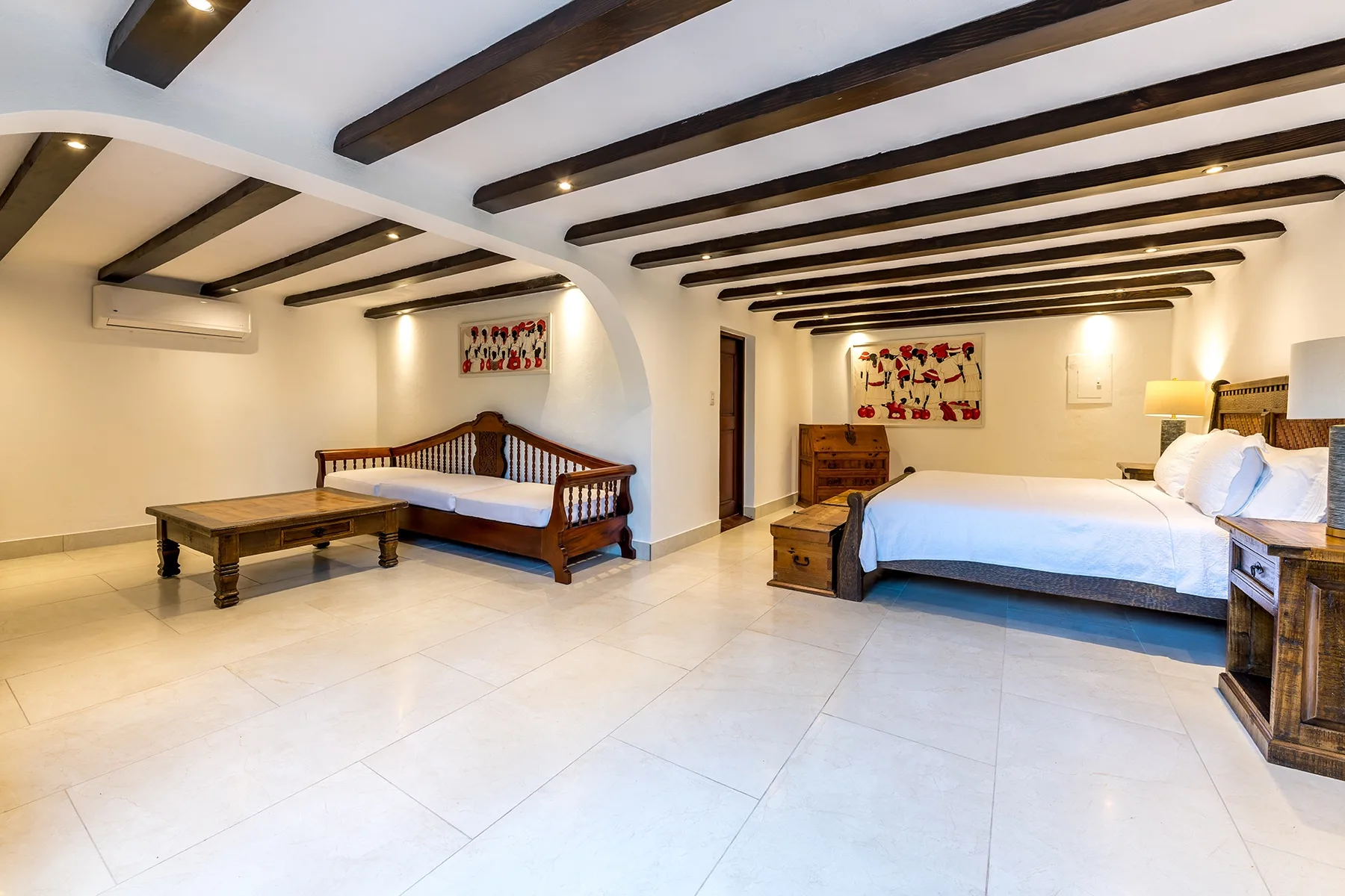 Un dormitorio con dos camas, vigas oscuras en el techo y una mesa de madera.