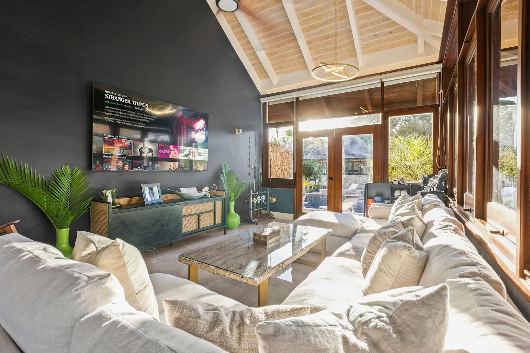 Una sala de estar luminosa con asientos alrededor de una mesa de centro y grandes ventanas.