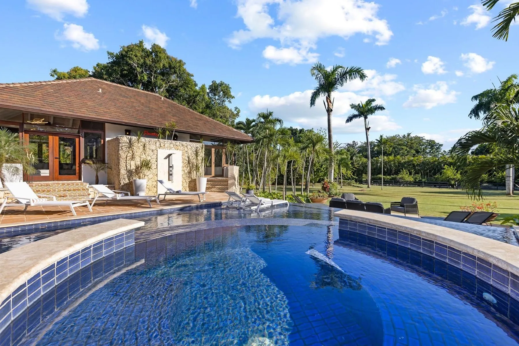 Una piscina curva junto a una casa, con asientos de descanso y palmeras.