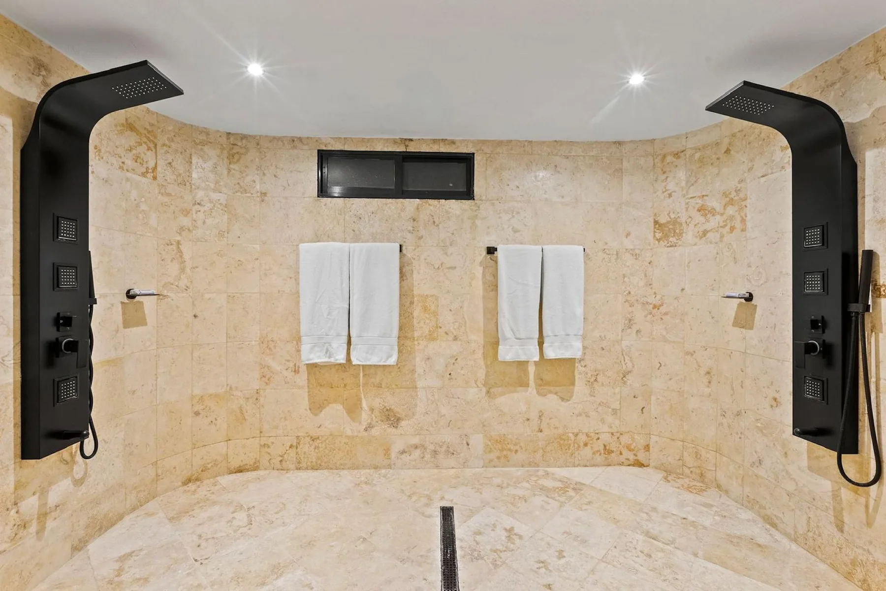 Una zona de ducha de baño revestida de azulejos, con paneles oscuros y toallas blancas.