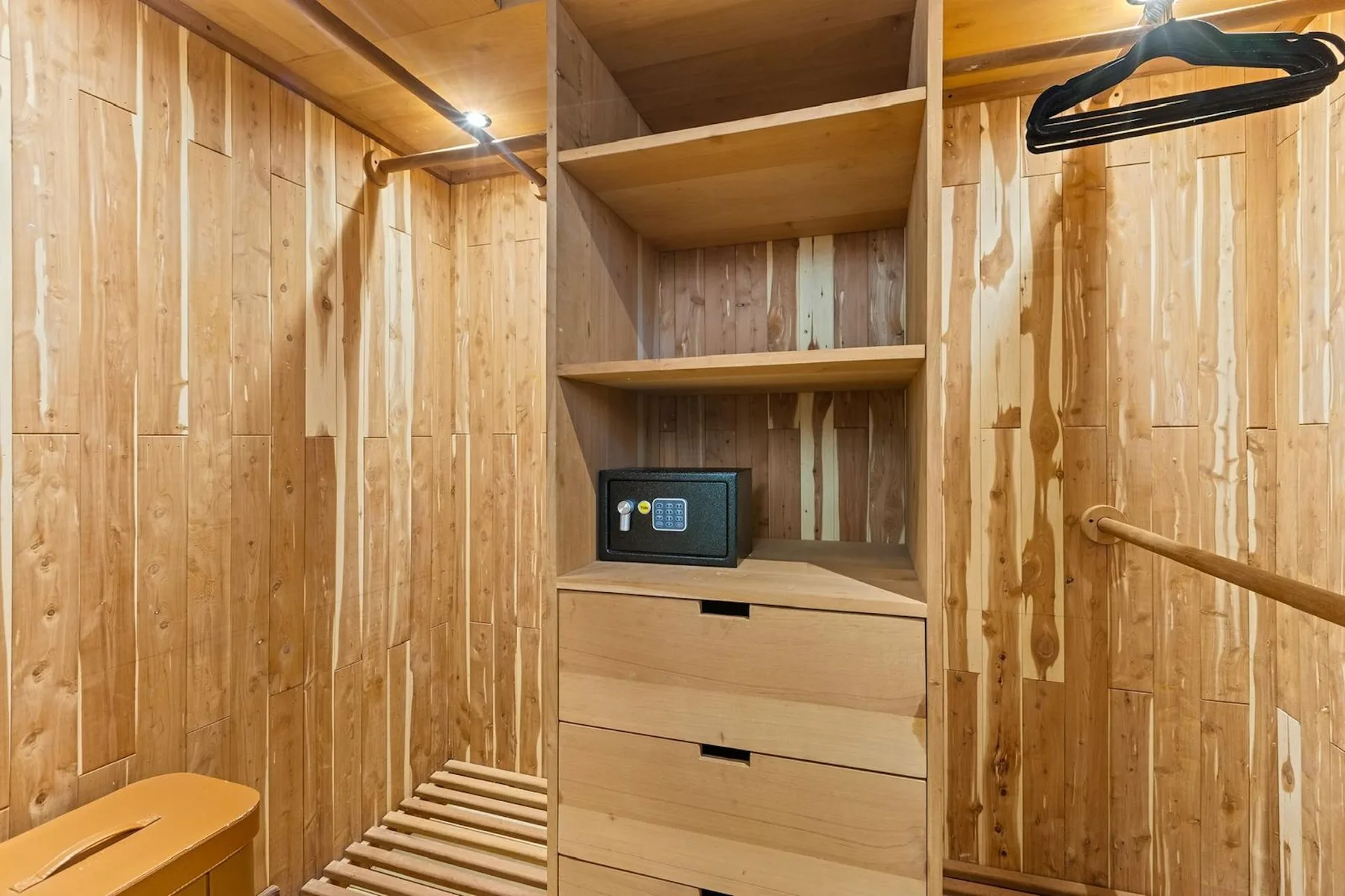 Un vestidor revestido de madera con estantes abiertos, cajones y un banco.