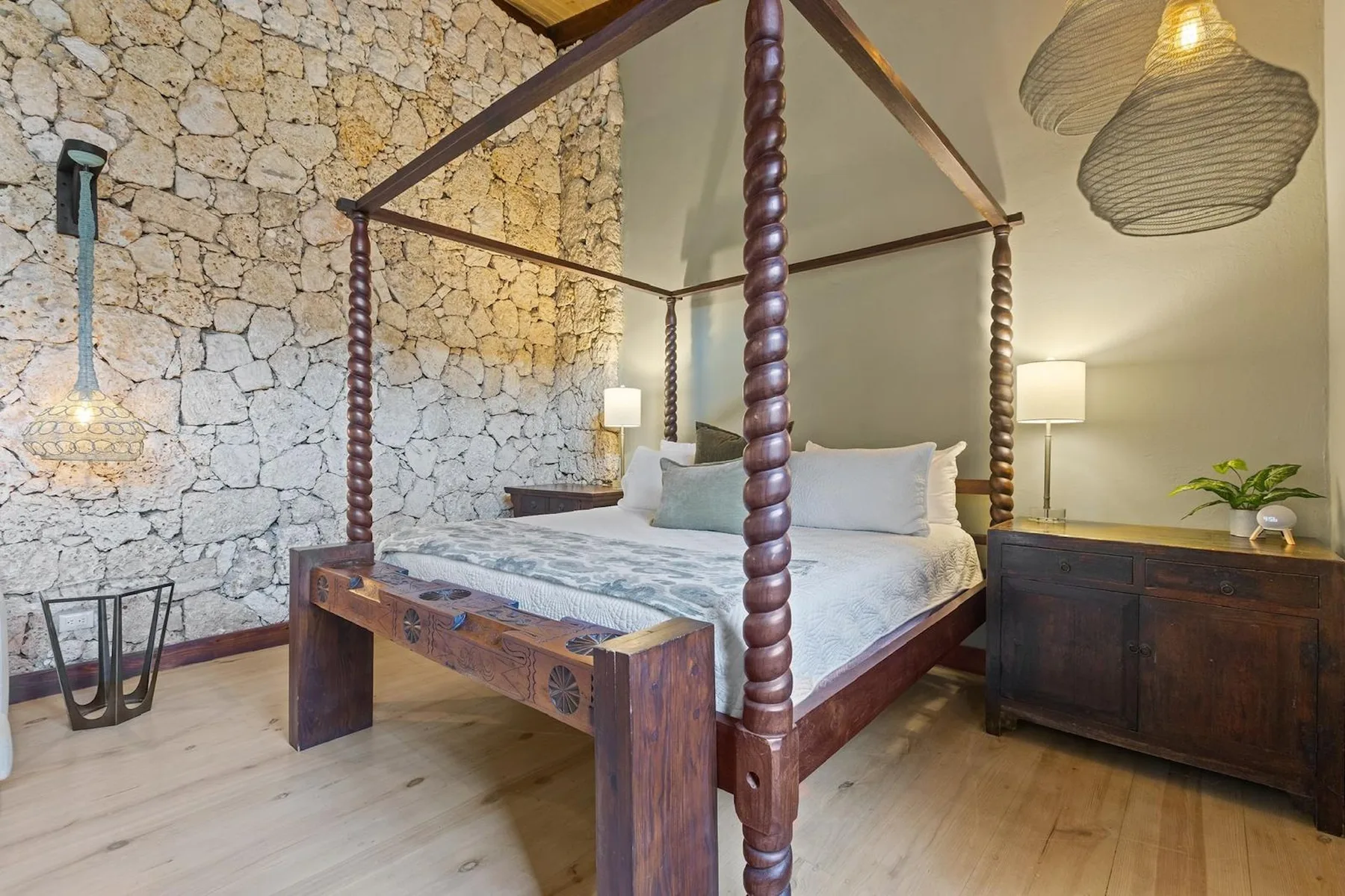 Un dormitorio con una cama con dosel de madera junto a una pared de piedra.