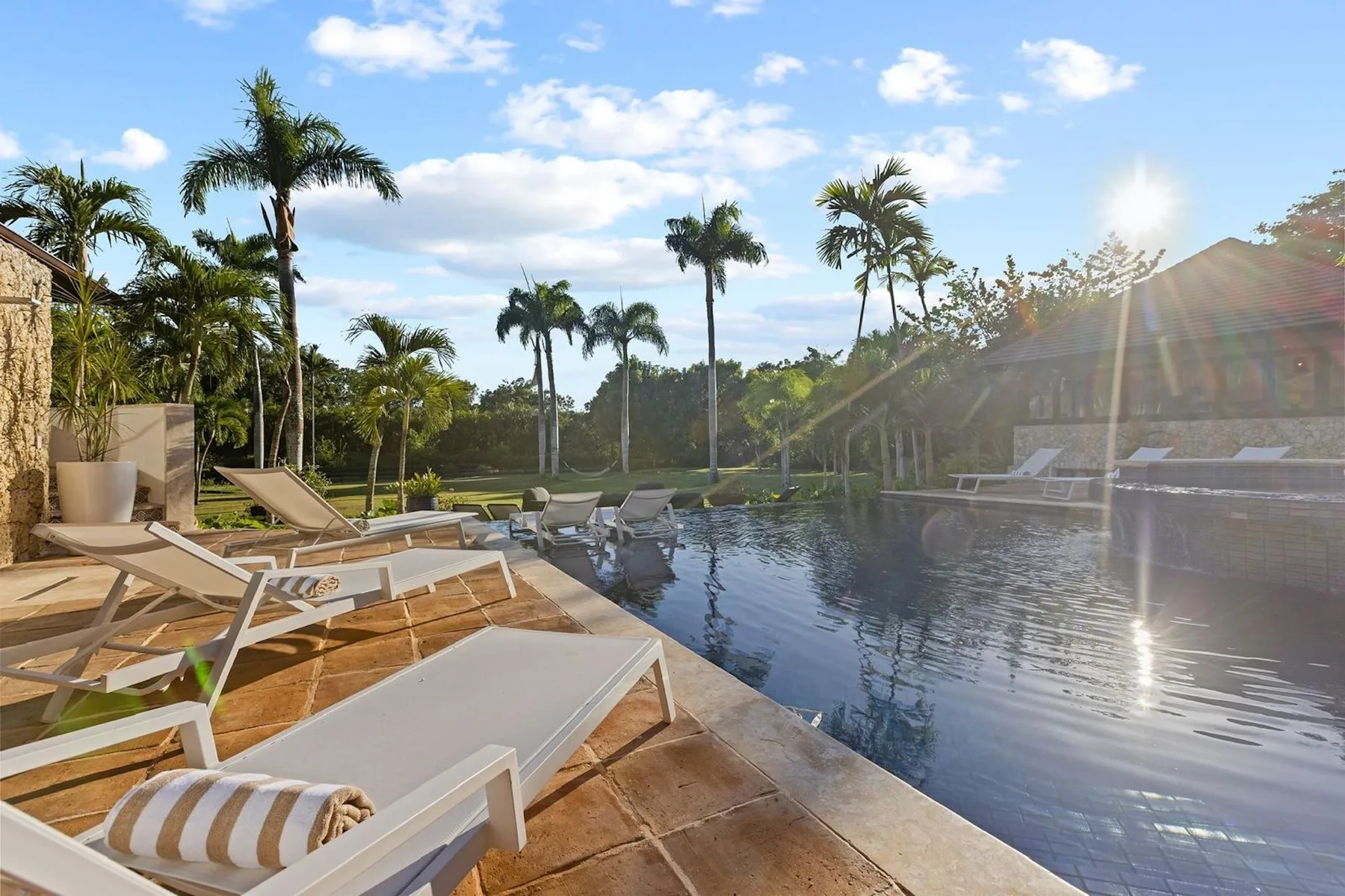 Una piscina al aire libre junto a una terraza de madera con asientos y palmeras.