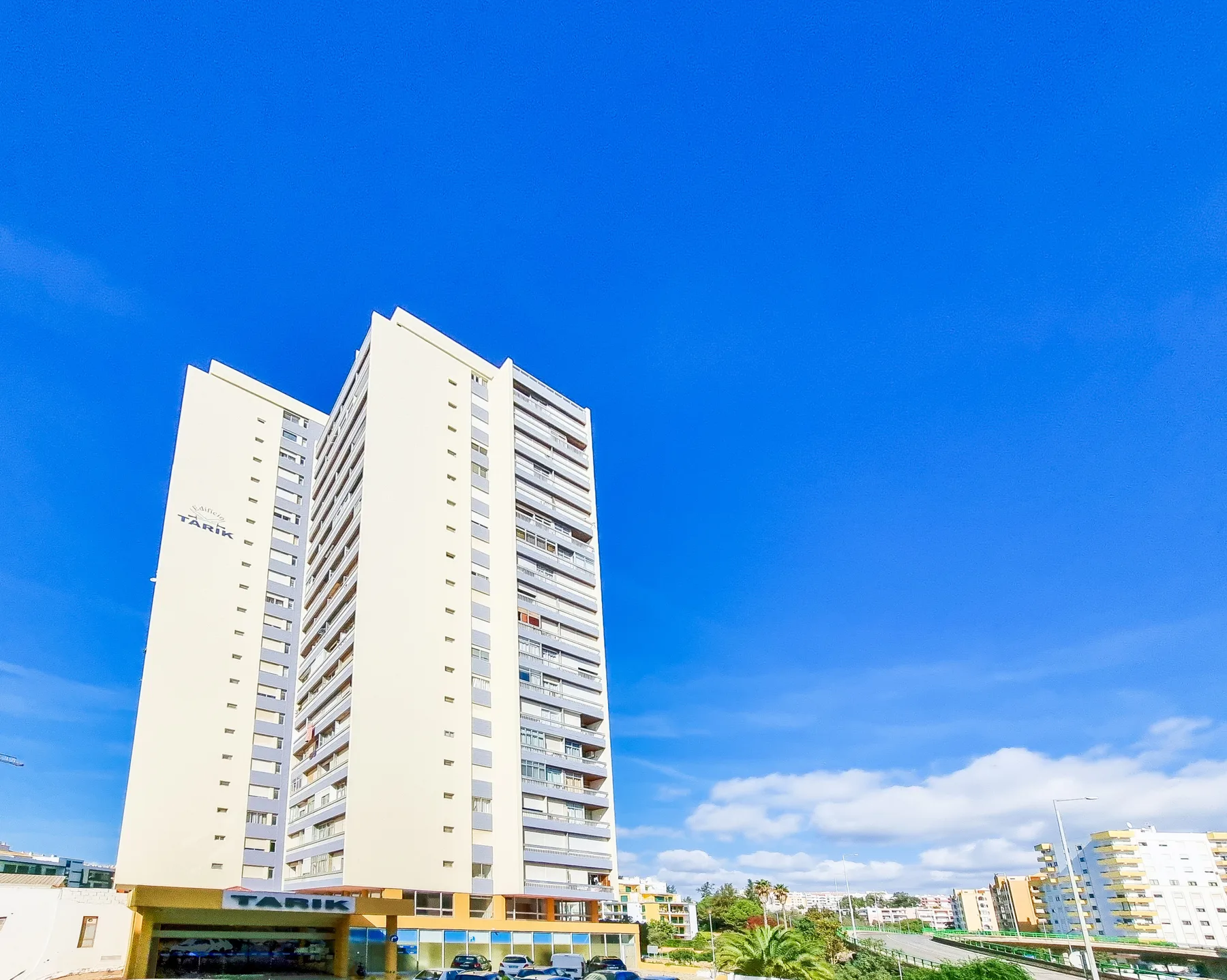 A tall apartment building stands beneath a clear blue sky.
