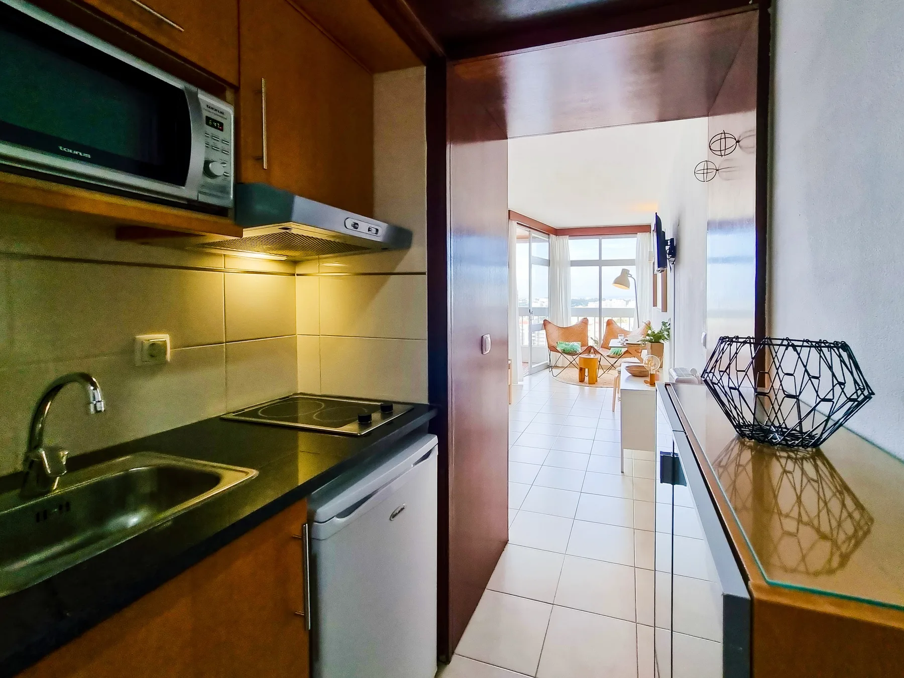 A compact kitchen opens into a bright living area with large windows.