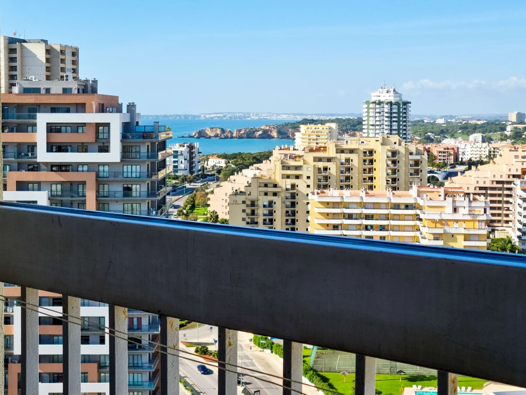 A balcony overlooks apartment buildings, a coastal bay, and the surrounding city.