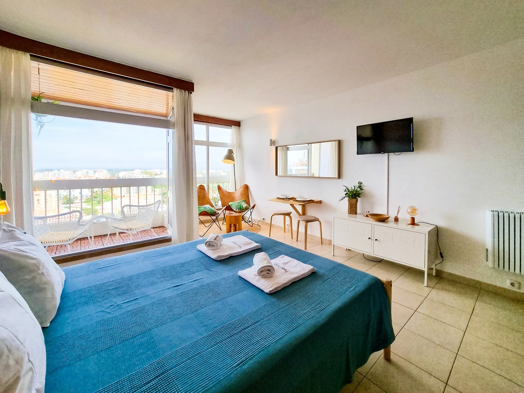 A bright bedroom with a bed facing a window and balcony.