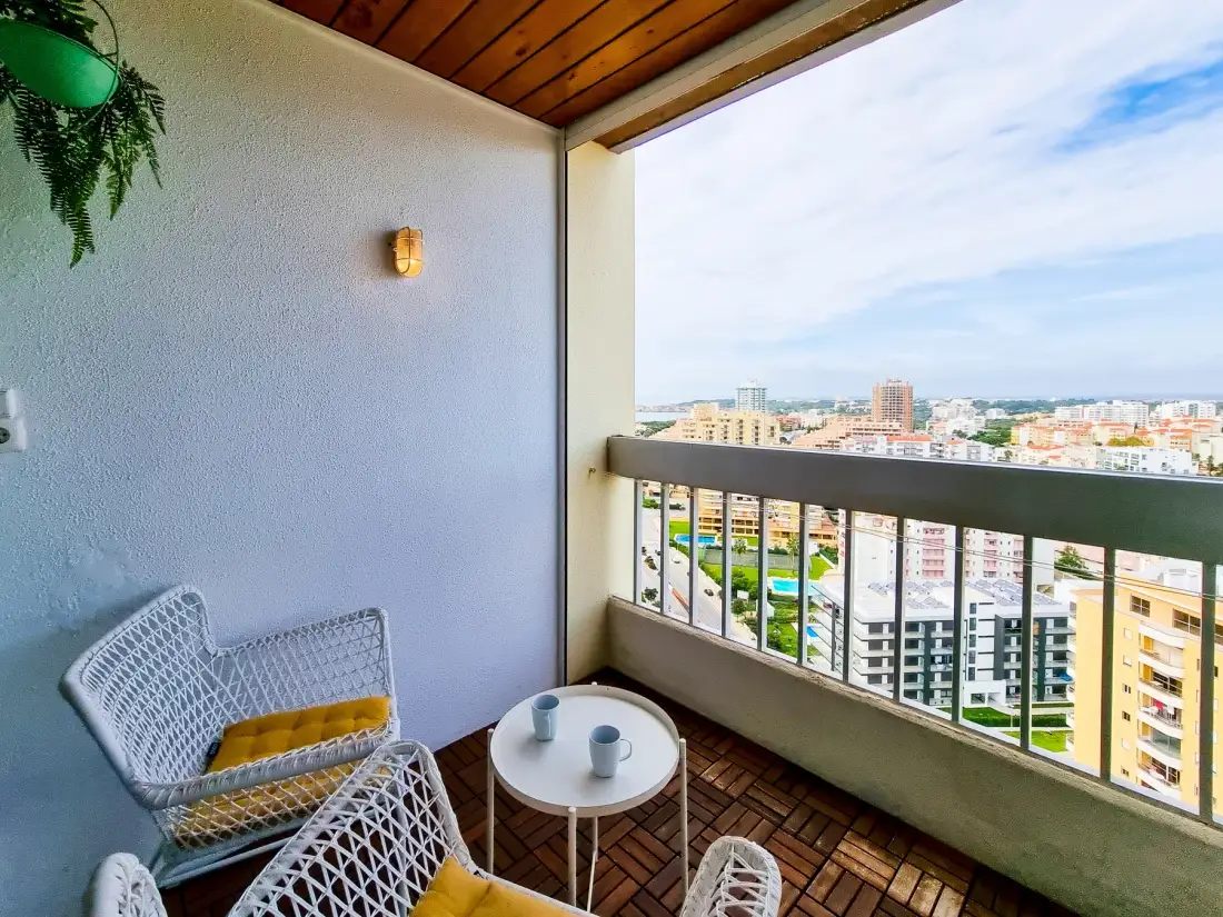 A covered balcony overlooks a city, with seating and a small table.
