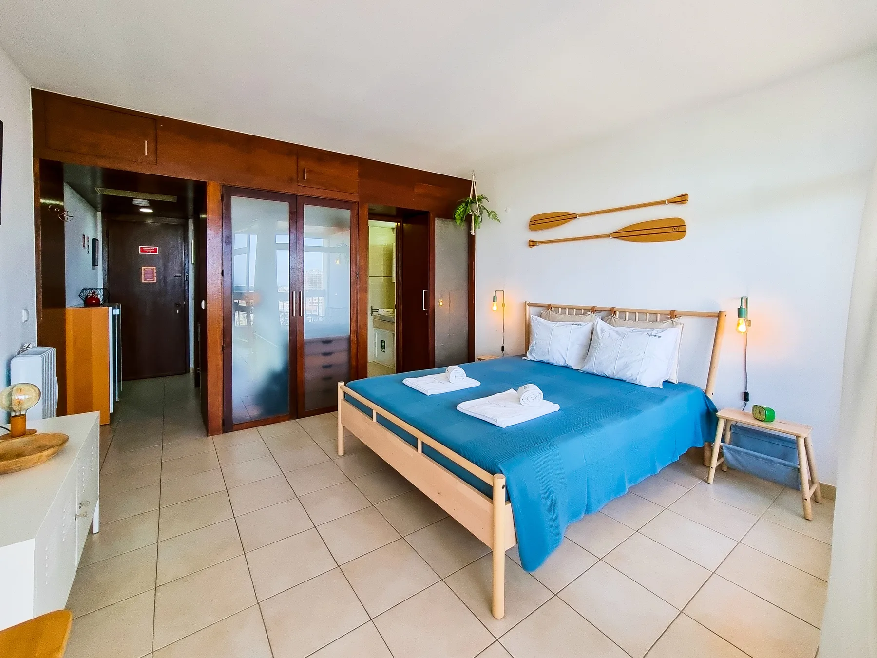 A bedroom with a bed covered in blue bedding beside wooden wardrobes.