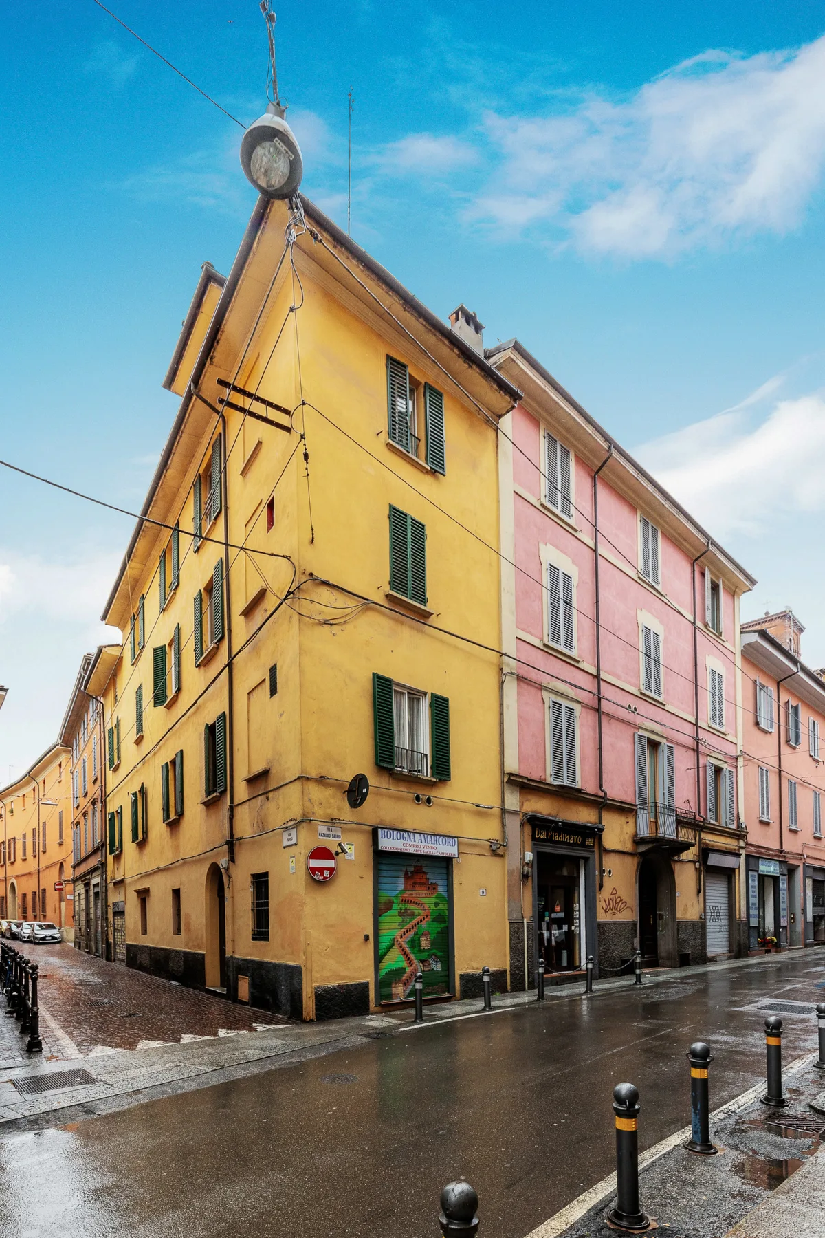 Una esquina con edificios coloridos y pavimento mojado bajo un cielo azul nublado.