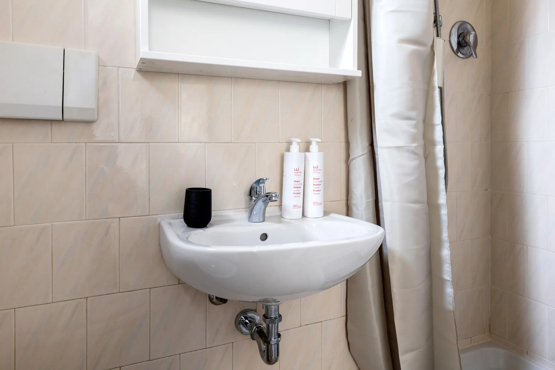 Un baño alicatado con un lavabo suspendido y una cortina de ducha.