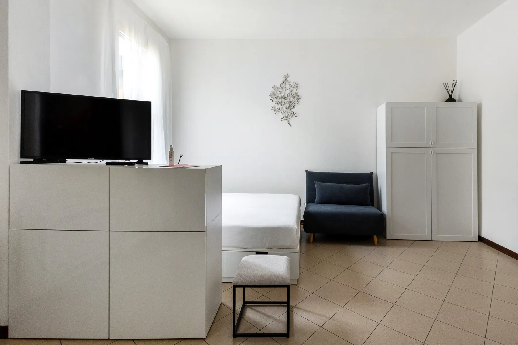 Una sala luminosa con televisor, asientos blancos y un sillón oscuro.