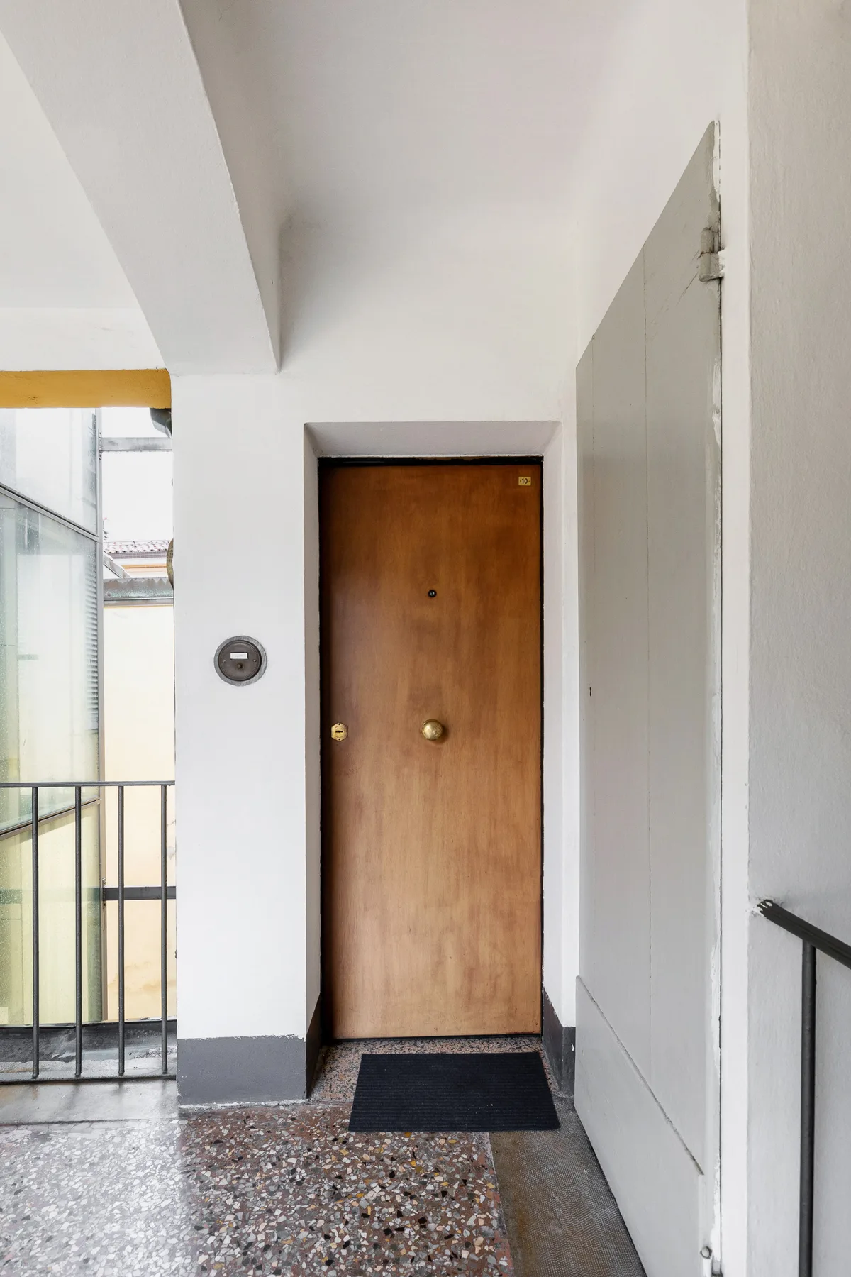 Una entrada de apartamento con una puerta de madera y un felpudo oscuro.