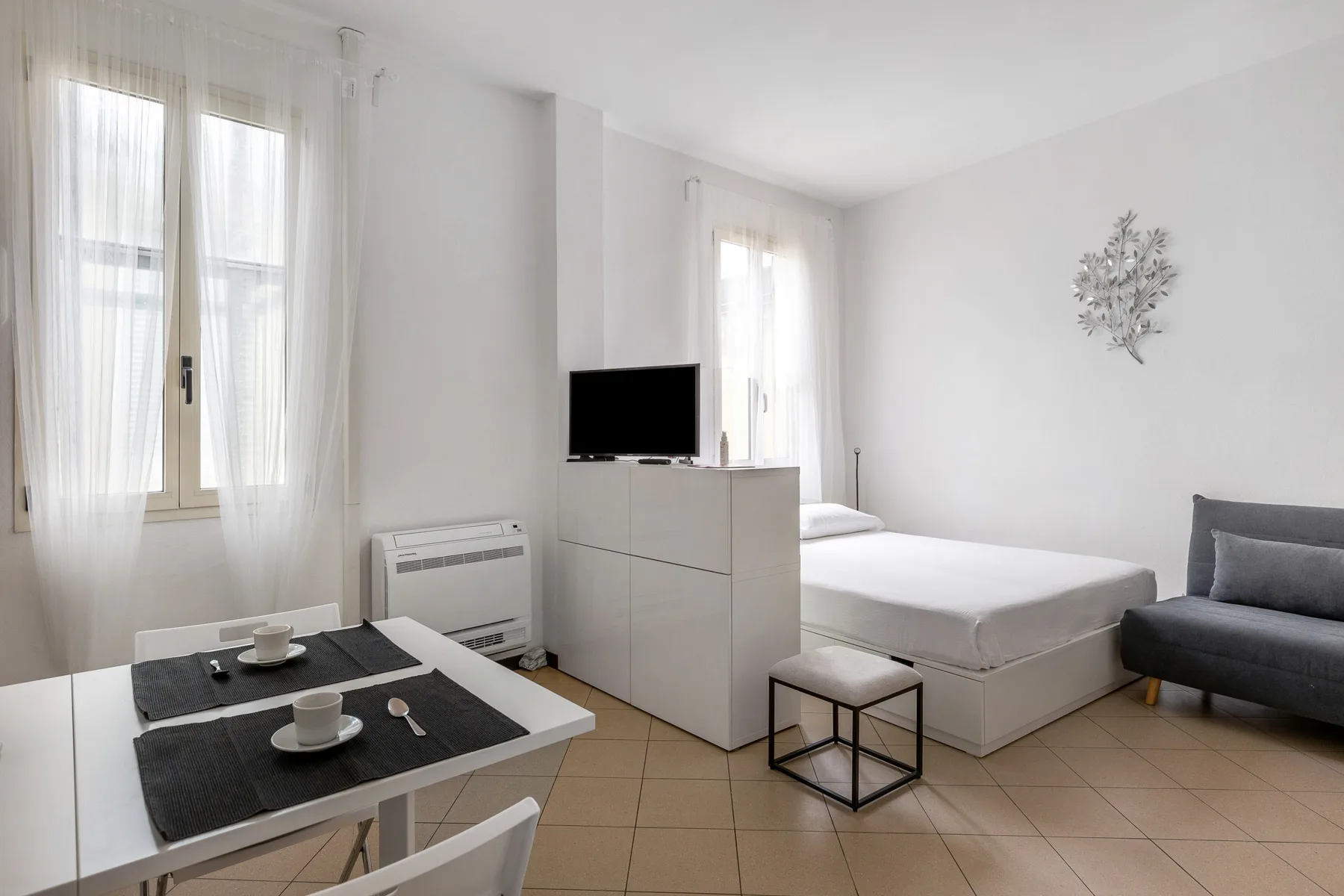Un dormitorio luminoso con cama, televisor y una pequeña mesa de comedor.
