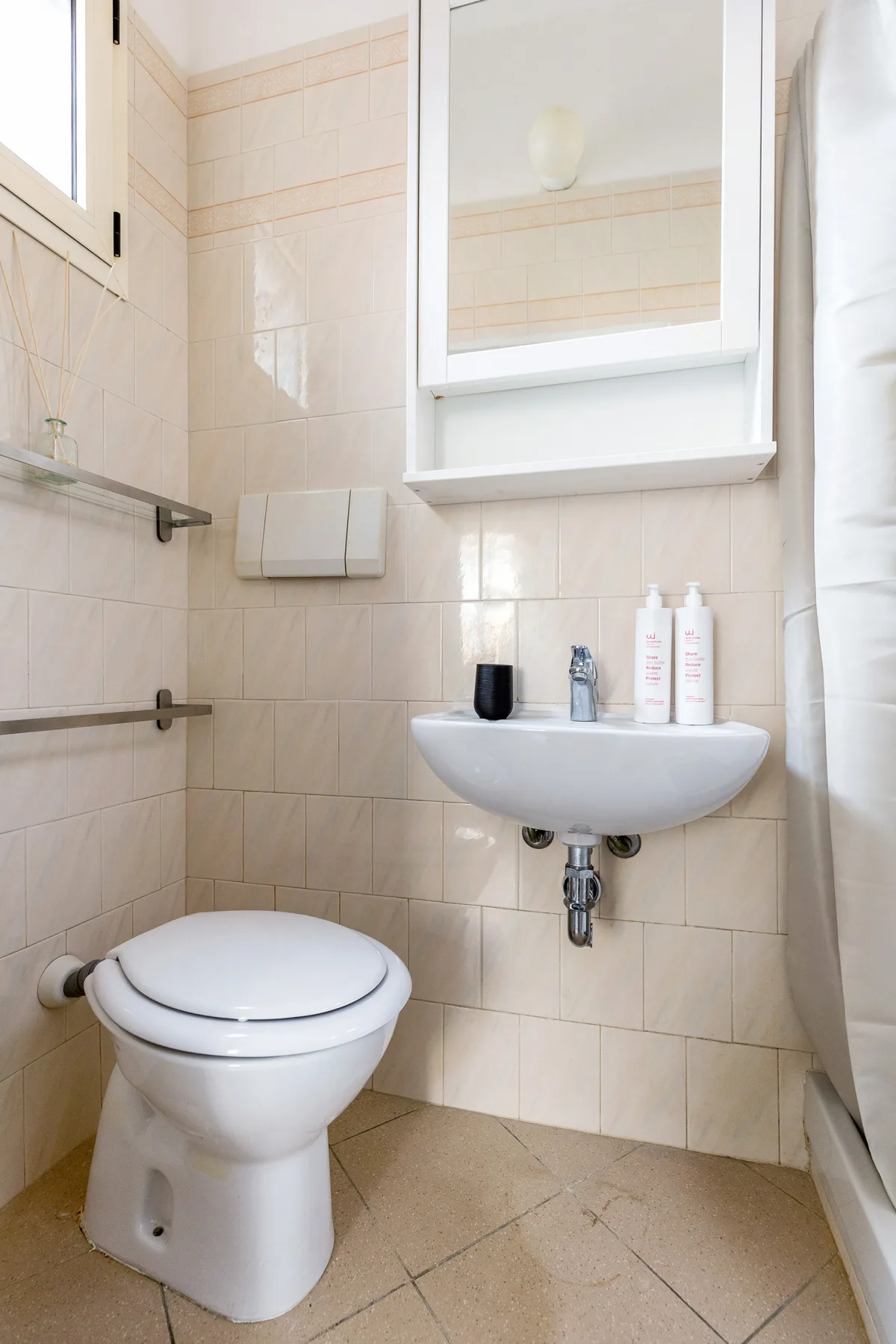 Un baño alicatado con inodoro, lavabo de pared y armario con espejo.