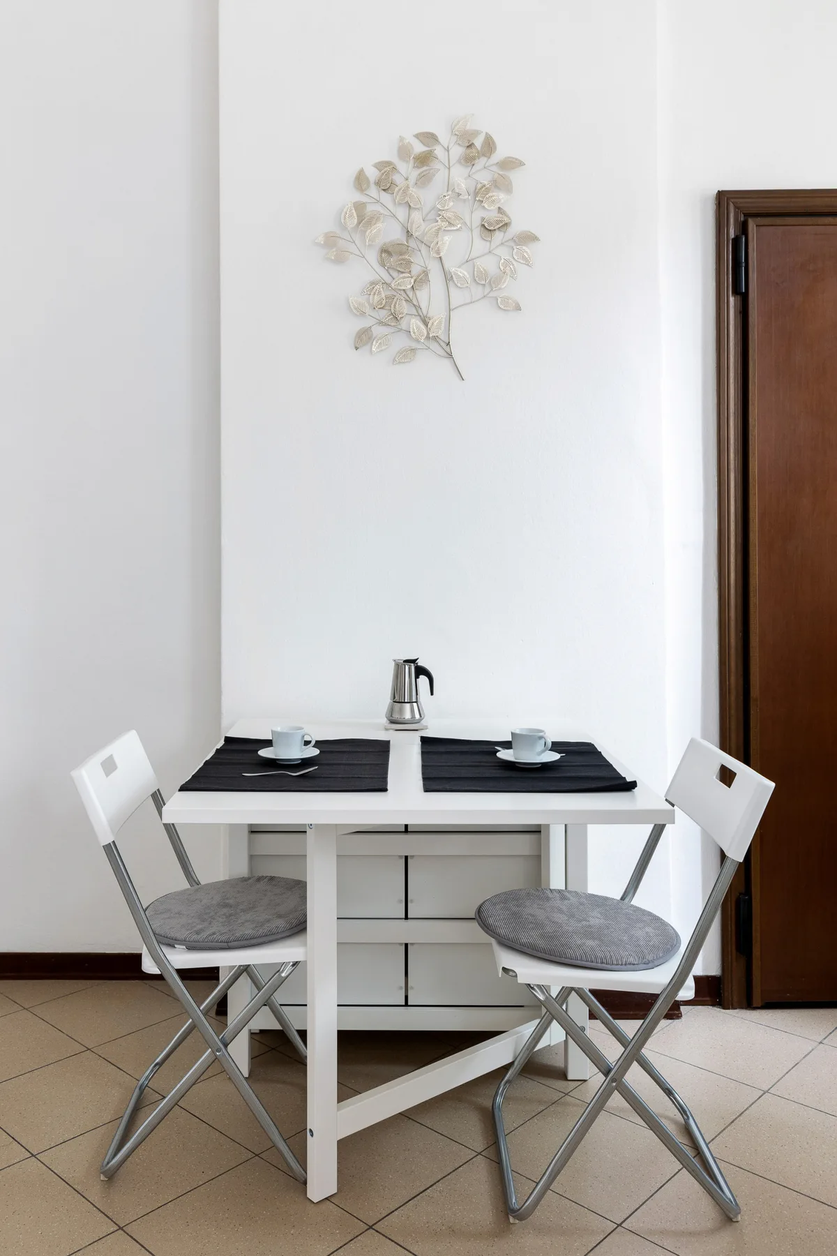 Un pequeño comedor con una mesa blanca, dos sillas y tazas.
