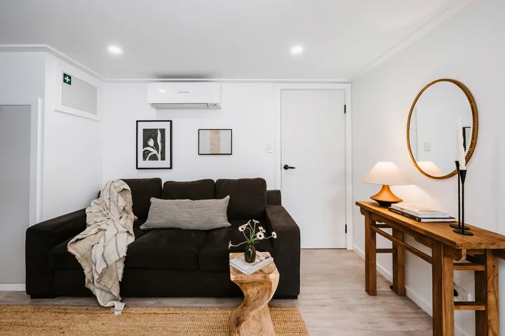 A living room with dark seating, a wooden table, and a round wall mirror.