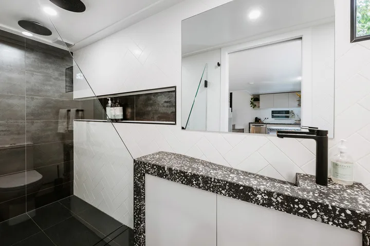 A modern bathroom with a glass shower and a dark speckled vanity countertop.