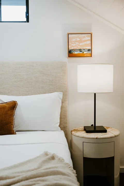 A bedroom with a neatly made bed and a bedside lamp.