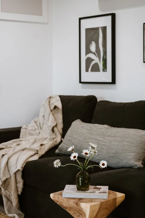 A living room with dark seating, framed wall art, and a small wooden table.