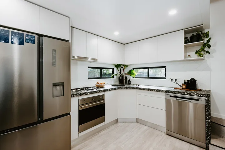 A bright modern kitchen with white cabinets and stainless steel appliances.