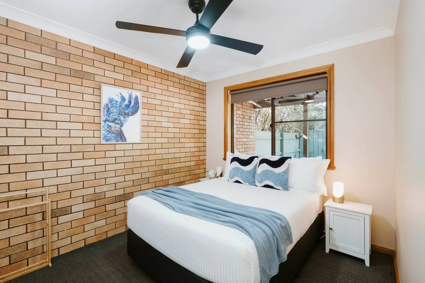 A bedroom with a bed, blue bedding, and a brick accent wall.