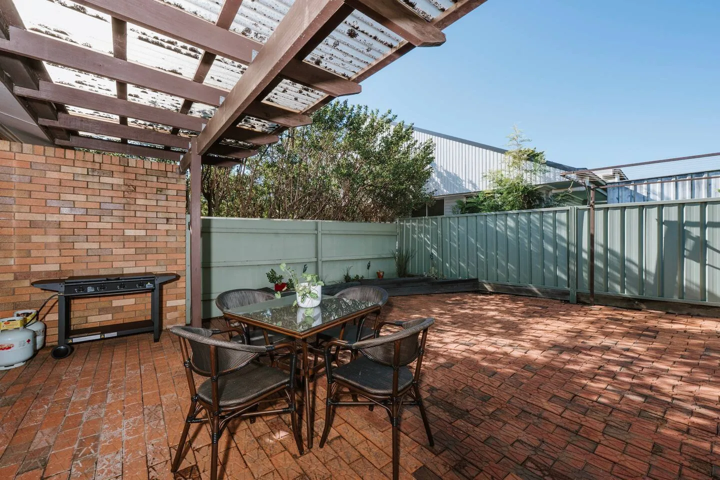A brick-paved patio has a dining table beneath a timber pergola.